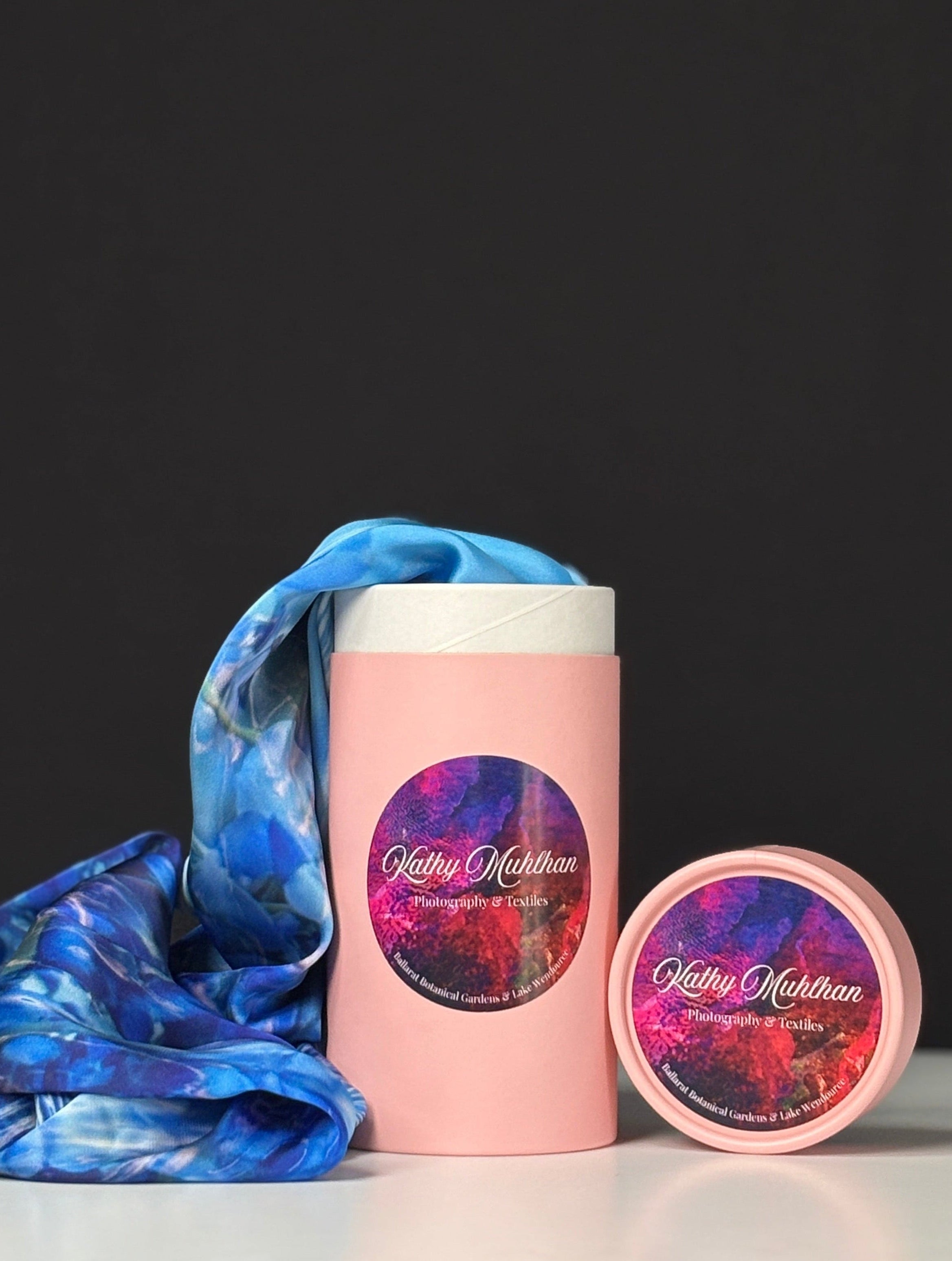 Pink cylindrical container with a blue scarf and smaller pink container on a black background