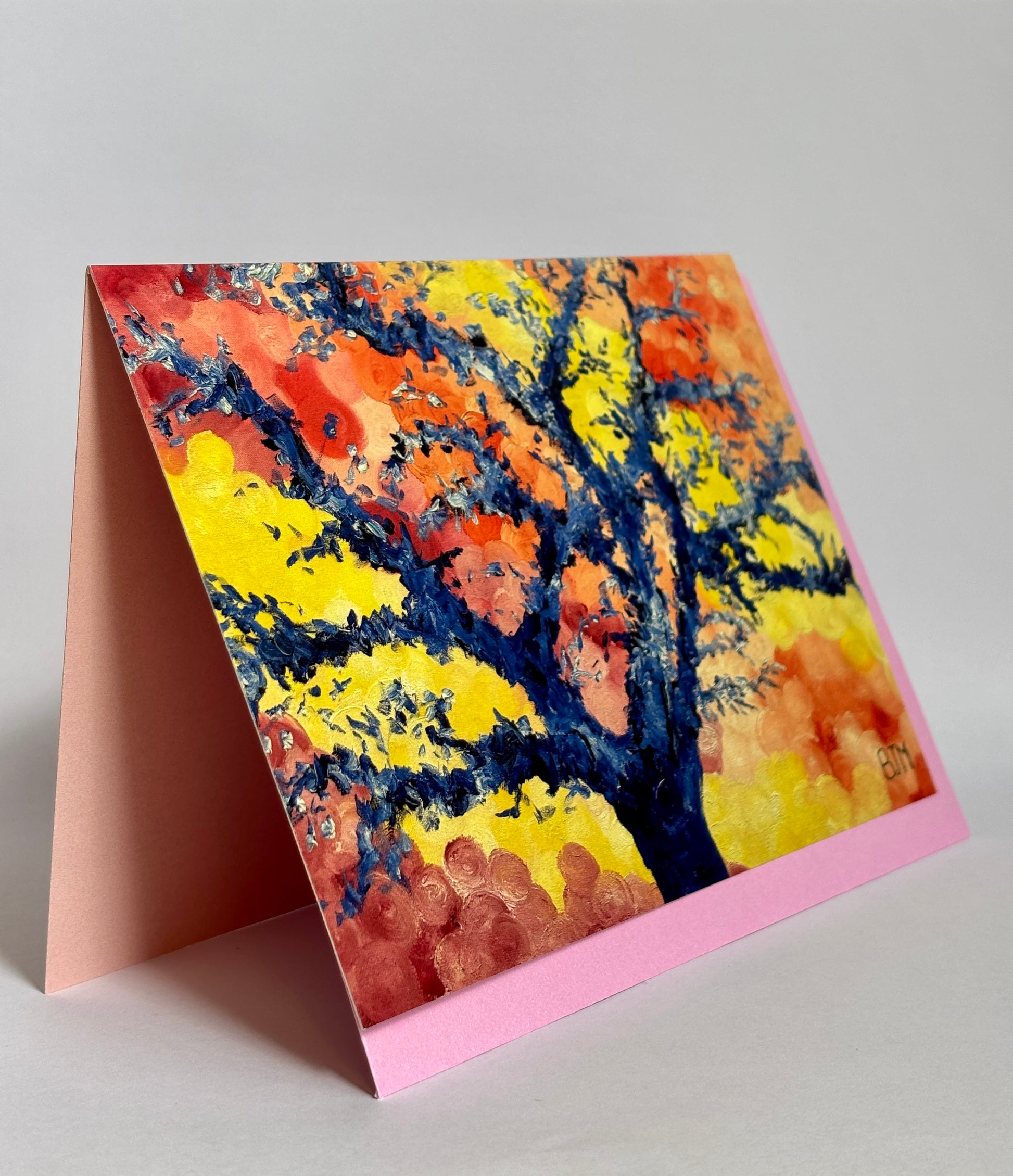 Colorful tree painting on a pink card with a stand against a gray background