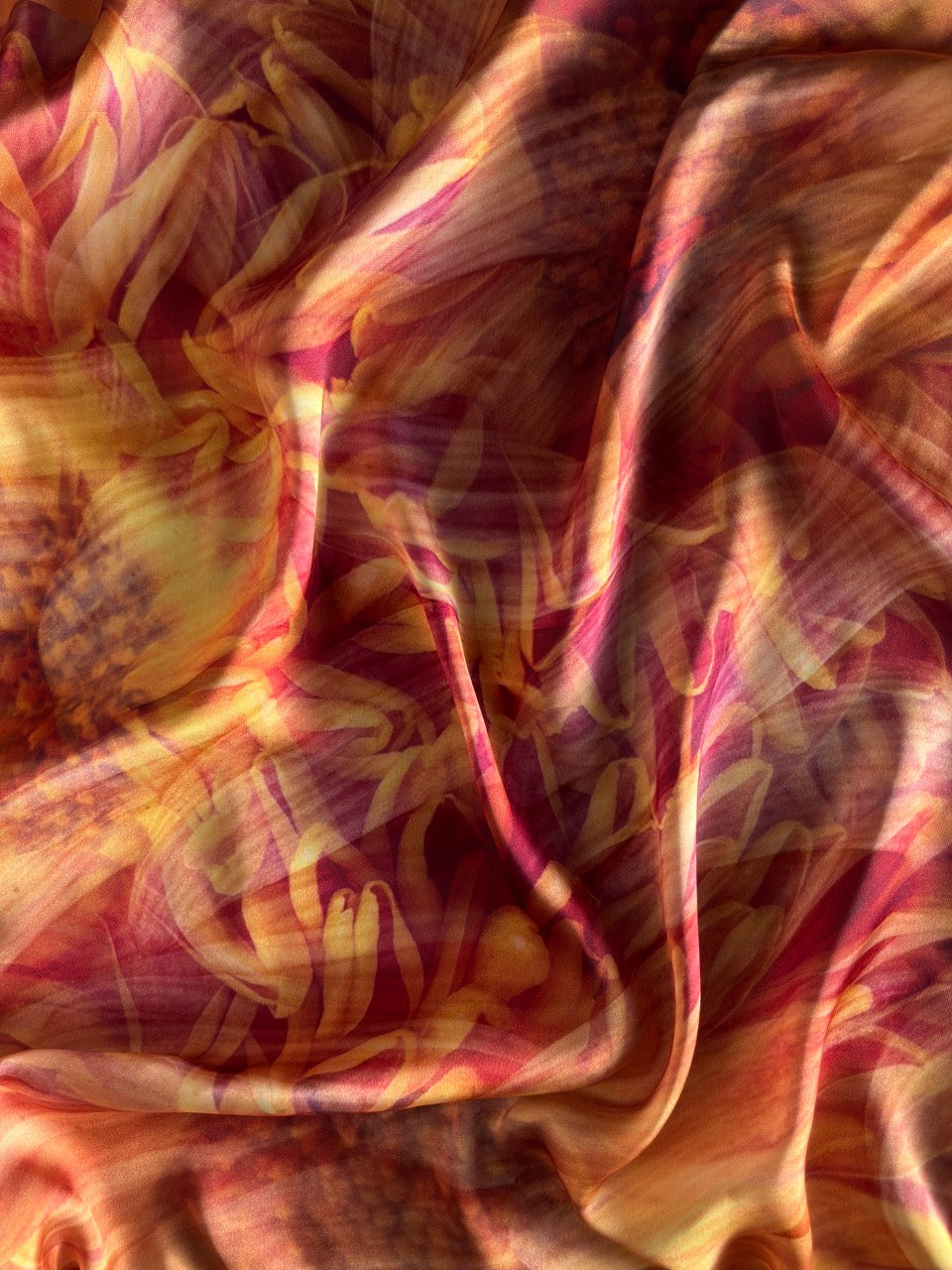 A close-up of draped fabric with an abstract floral or marbled pattern in warm tones, including pink, orange, yellow, and brown.