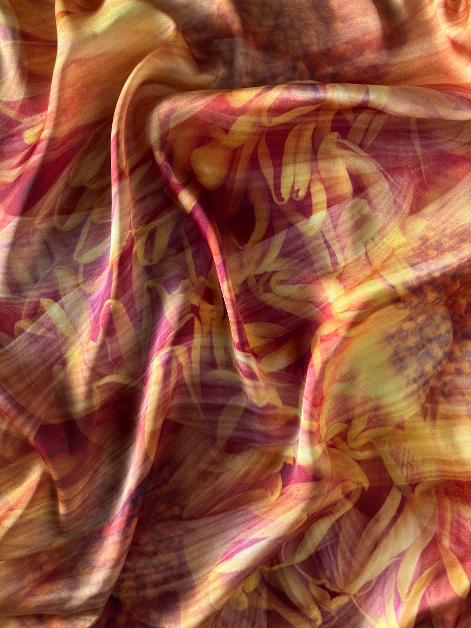 A close-up of draped fabric with an abstract floral or leaf-like pattern in warm tones, including pink, red, yellow, and orange, with no visible person, animal, or real environment.
