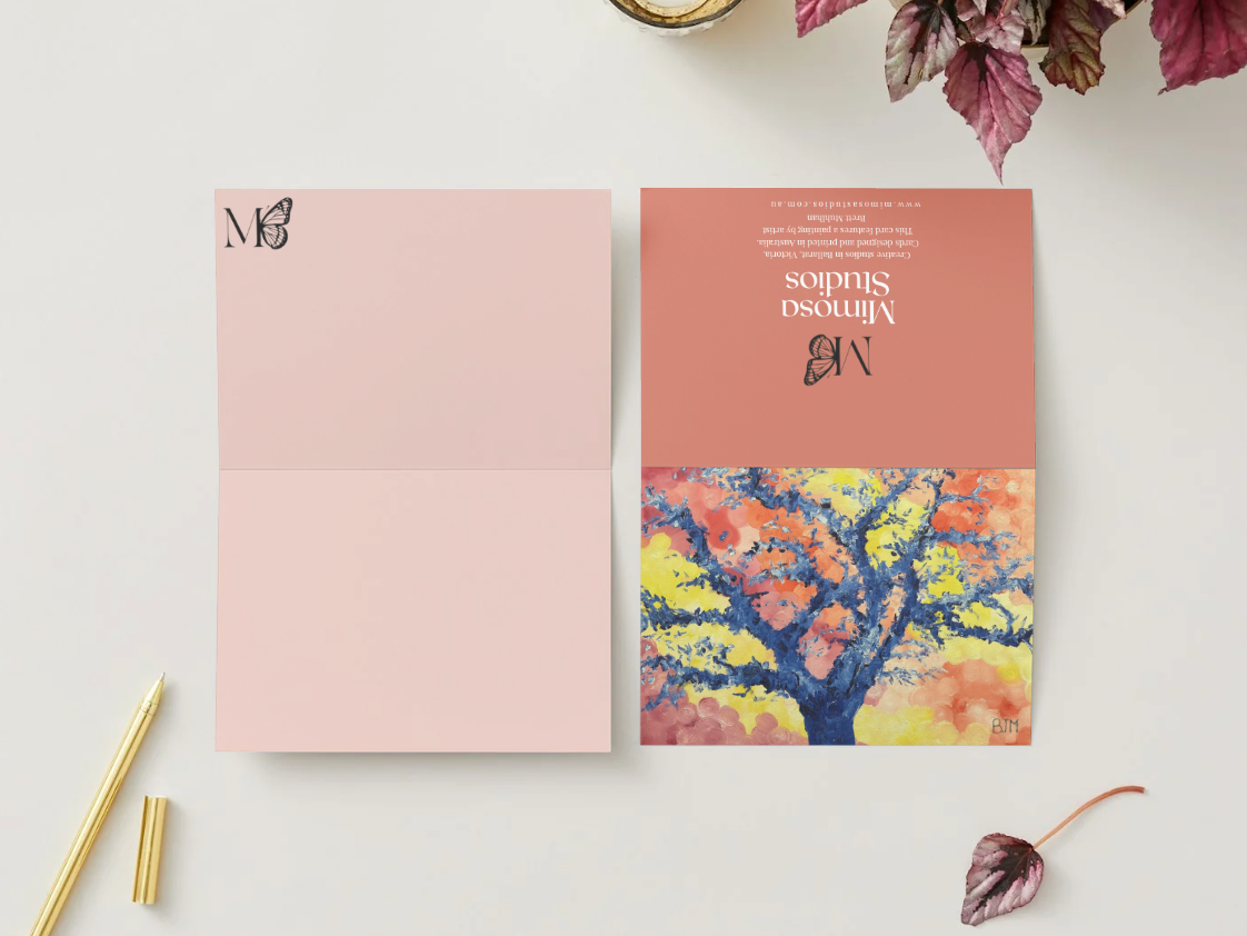 Stationery set with a pink envelope and a card featuring a colorful tree design on a light surface.